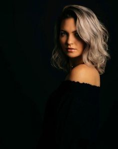 a woman with blonde hair is posing for a photo in the dark, wearing an off - shoulder black top