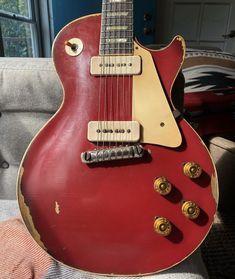 an old red electric guitar sitting on top of a couch in front of a window