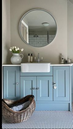 a white sink sitting under a round mirror in a bathroom next to a blue cabinet