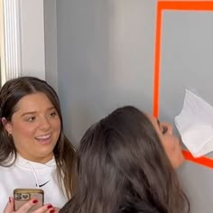 two women standing next to each other in front of a mirror and one holding a cell phone