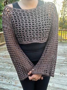 a woman is wearing a crocheted sweater and black leggings while standing on a deck