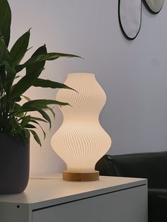 a white lamp sitting on top of a table next to a potted plant