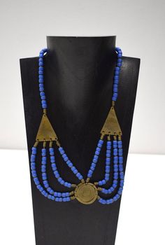 This is a Old 1960 African Turkana Brass Round and Triangle Multi Strand Beaded Necklace with Blue Glass from Kenya. The necklace is strung on wire with a a brass hook and eye clasp.  A wonderful gift for a woman or man. Necklace 20" Long 30mm Round Brass Pendant 36mm Long Triangle Beads 6mm Round Blue Beads AT BACARA WE STAND BEHIND ALL OF OUR MERCHANDISE. WE CAN PROVIDE REFERENCES FOR ALL ARTIFACTS THAT WE SELL, AS WELL AS DOCUMENTATION TOWARD THEIR AUTHENTICITY. FULL MONEY BACK GUARANTEE WILL BE PROVIDED FOR DISSATISFIED CUSTOMERS. YOUR SATISFACTION IS OUR MAIN GOAL, AND WE THANK YOU FOR SHOPPING AT THE WORLD OF BACARA. G323 #22 Blue Vintage Necklace For Festival, Vintage Blue Jewelry For Festivals, Blue Vintage Jewelry For Festivals, Traditional Blue Brass Jewelry, Blue Brass Amulet Necklace, Blue Beaded Brass Necklaces, Blue Brass Jewelry For Festivals, Adjustable Brass Necklace With Polished Beads, Blue Brass Jewelry For Jewelry Making