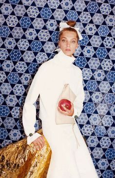 a woman in a white dress holding an apple and gold bag with blue tiles behind her