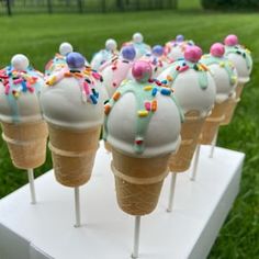 several ice cream cones with sprinkles are on a white stand in the grass