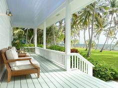 a porch with two chairs on it and palm trees in the background