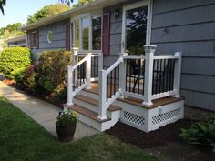 a house with some plants and flowers in the front yard, next to it is a deck