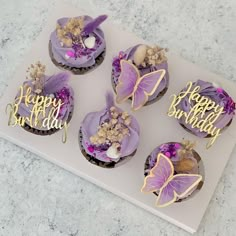 cupcakes decorated with purple icing and gold decorations on a white plate that says happy birthday