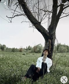 a man sitting in the grass under a tree