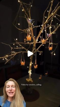 a woman standing in front of a tree with lights on it and candles hanging from the branches