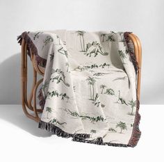 a white and green dinosaur print blanket sitting on top of a chair