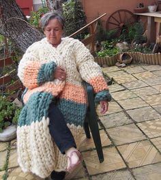 an older woman sitting on a chair in the yard wearing a sweater and slippers