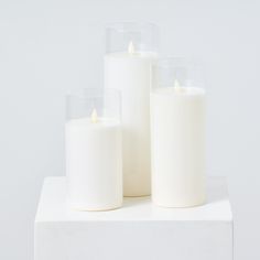 three white candles sitting on top of a white table next to each other in front of a white wall