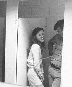 a man and woman standing in a bathroom next to each other, one is pulling the door open