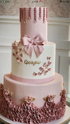 a three tiered cake with pink flowers and bows on the top is decorated in white, pink and gold