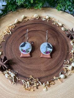 two white and pink ceramic earrings sitting on top of a piece of wood next to leaves