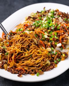 a white plate topped with noodles, meat and veggies next to a fork