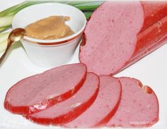 sliced ham and vegetables on a white plate with a bowl of peanut butter next to it