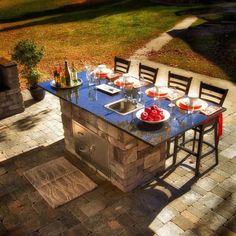 an outdoor dining table with chairs and a grill in the middle is surrounded by brick pavers