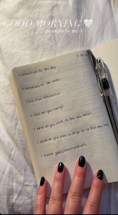 a woman's hand holding a pen next to an open book with writing on it