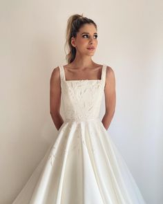 a woman in a white wedding dress standing against a wall with her hands on her hips