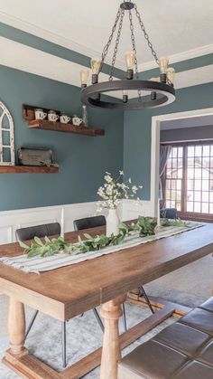 a dining room table with candles and greenery on it, in front of a blue wall