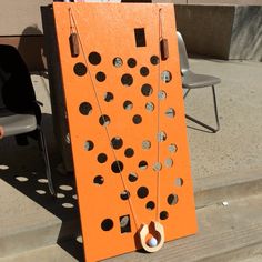 an orange board game sitting on the side of a sidewalk next to a chair and table