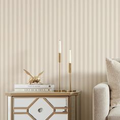 a white and gold side table with two candles on it next to a beige striped wall