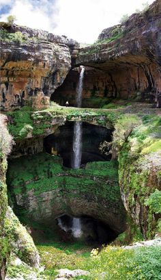 a small waterfall in the middle of a large canyon with green grass and rocks on either side