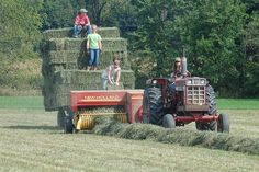 two people are standing on the back of a tractor with hay bales attached to it