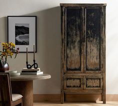 a room with a table, chair and armoire next to a painting on the wall