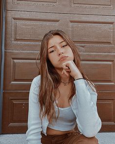 a woman sitting in front of a garage door with her hand on her chin and looking at the camera