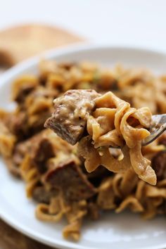 a fork full of noodles and meat on a white plate with bread in the background