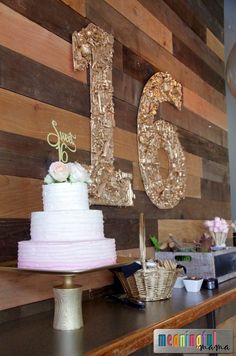 a table topped with a white cake next to a wooden wall covered in gold numbers