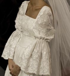 a woman in a wedding dress and veil standing next to a man wearing a suit