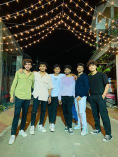 a group of young men standing next to each other in front of a string of lights