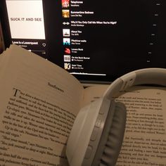 an open book with headphones on top of it next to a computer monitor and keyboard