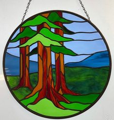 a circular stained glass window with trees in the middle and mountains in the back ground