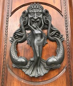 a wooden door with a metal mermaid on it's face and two fish around its neck