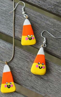 two necklaces with candy corn on them are sitting on a wooden bench next to a pair of earrings