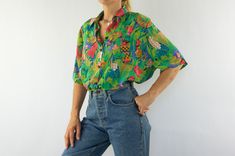 Vintage blouse - Kramik Made in Belgium 1980s Shiny blouse with colorful floral jungle animal pattern on green background . Straight cut. Oversize. Shirt collar. Short sleeves. Buttoned chest pocket. Rounded bottom .  6 buttons . In very good condition. To note: Missing button on collar. The price takes into accout its flaws. Without composition label. Shiny fluid fabric Size label: M The model wears usually a size S (EU 36-38) and measures 170cm - 66,9".       . Measures (flat):  Shoulders: 42c Vintage Multicolor Blouse With Vibrant Print, Tropical Printed Button-up Top, Green Tropical Print Button-up Shirt, Tropical Floral Print Button-up Top, Shiny Blouse, Multicolor Vintage Print Button-up Top, Vintage Tropical, Jungle Print, Print Blouse