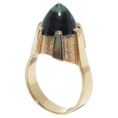 This vintage ring features an 18 karat gold band with a unique textured setting. The setting is sculpted with geometric, angular patterns that cradle the green synthetic spinel. The spinel is cabochon cut, displaying a smooth, domed surface. The band narrows slightly as it approaches the setting, adding to its elegant design. The ring's shape resembles a sleek, futuristic tower, or you could imagine it as a delicate crown. This ring would pair beautifully with a tailored emerald green blazer and Futuristic Tower, Vintage Cocktail Ring, Spinel Ring, 18k Gold Earrings, Green Blazer, Ring Shapes, Citrine Ring, 18k Yellow Gold Ring, Gold Plated Rings