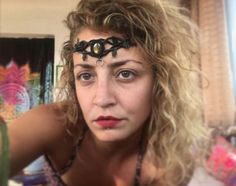 a woman with curly hair wearing a black headband and looking at the camera while standing in front of a mirror