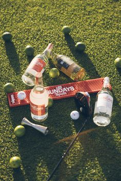 bottles and golf equipment on the ground with balls in the grass behind them, including an orange marker