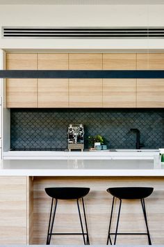 two stools sit at the bar in this modern kitchen with white countertops and wood paneling