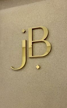 the j b logo is shown in gold on a beige wall with small squares around it