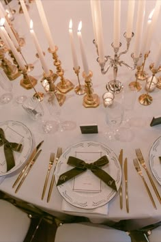 a white table topped with plates and silverware next to tall gold candlesticks