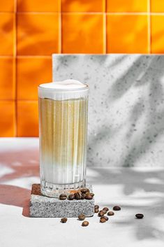 a tall glass filled with liquid sitting on top of a table next to coffee beans