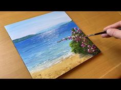 someone is painting flowers on the beach with water and sky in the backgroud