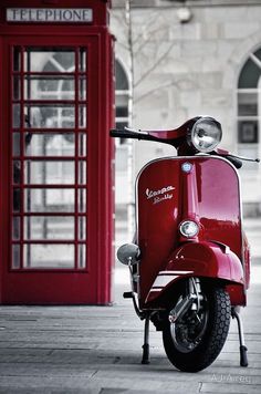 a red scooter parked in front of a phone booth